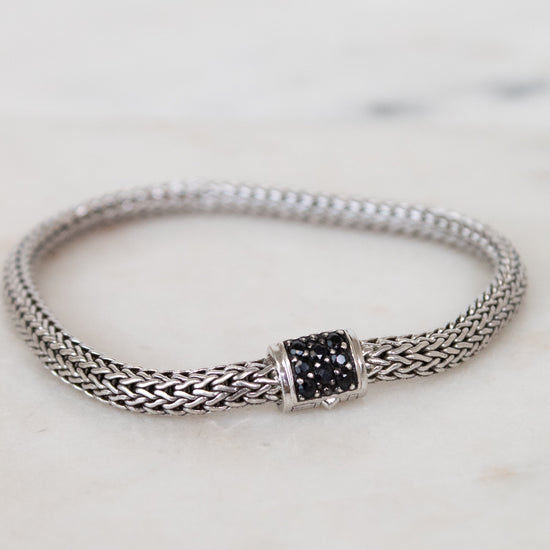 Silver bracelet with black gemstone clasp on a marble surface