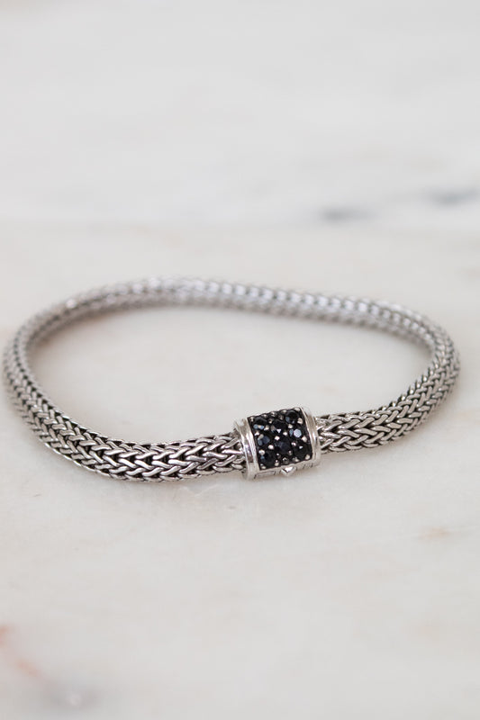 Silver bracelet with black gemstone clasp on a marble surface