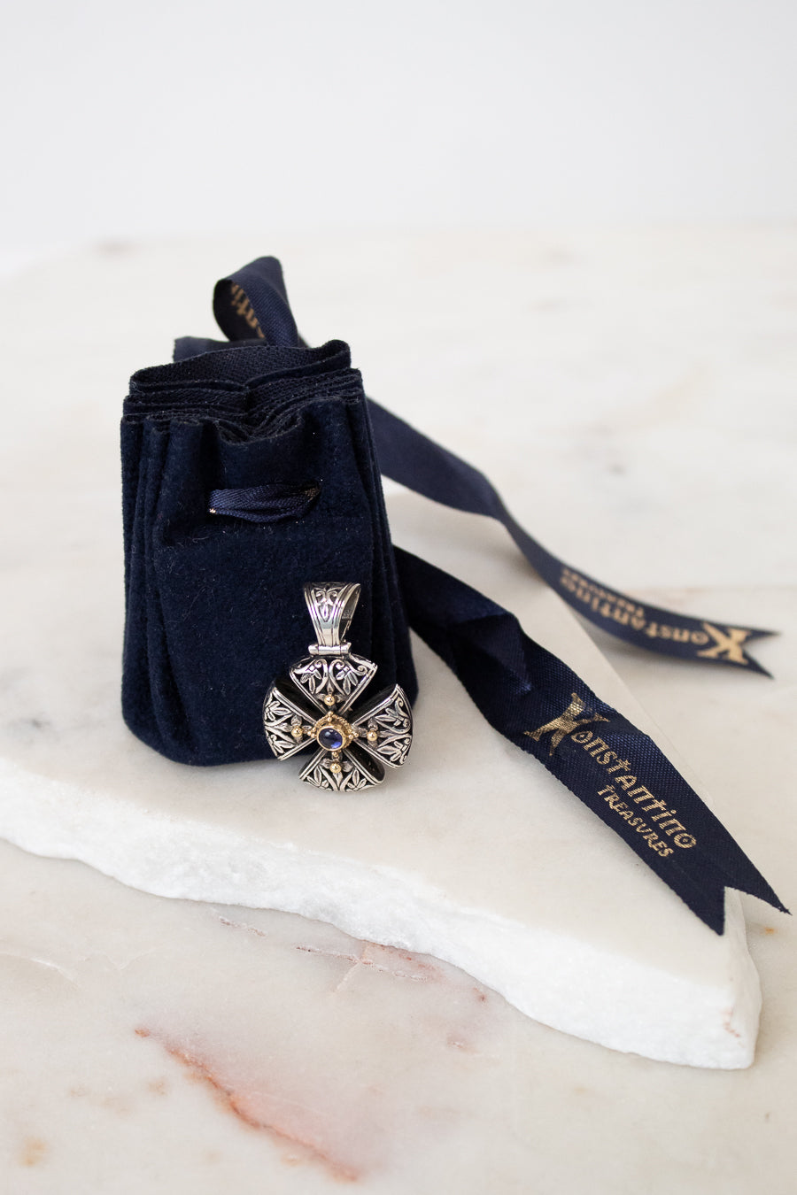Silver and gold cross pendant leaning on navy dust bag on white marble background