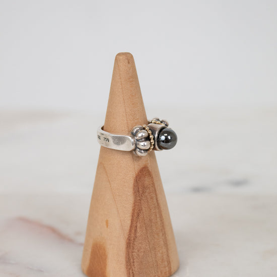 Silver ring with a black stone on a wooden cone against a light background