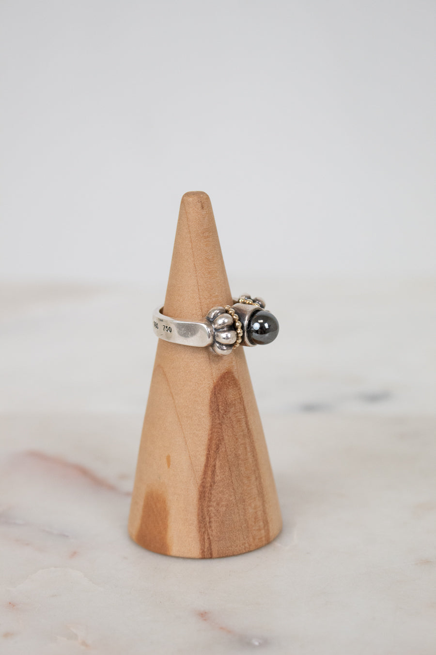 Silver ring with a black stone on a wooden cone against a light background