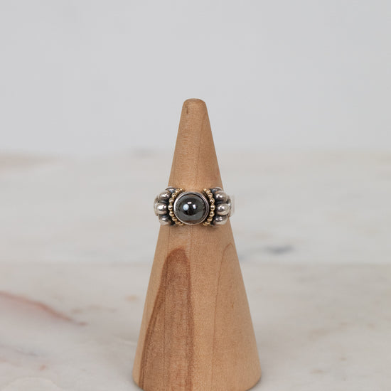 Silver ring with a dark stone on a wooden cone against a light background