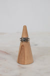 Silver ring with a dark stone on a wooden cone against a light background