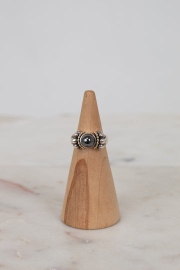Silver ring with a dark stone on a wooden cone against a light background
