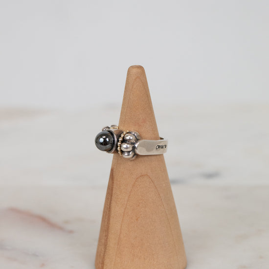 Silver ring with a black gemstone on a wooden cone against a marble background