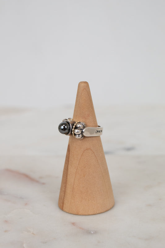 Silver ring with a black gemstone on a wooden cone against a marble background