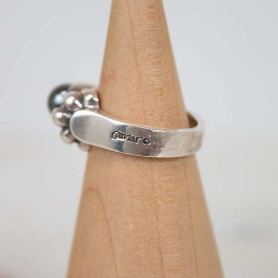 Silver ring with engraved text on a wooden stand against a light background