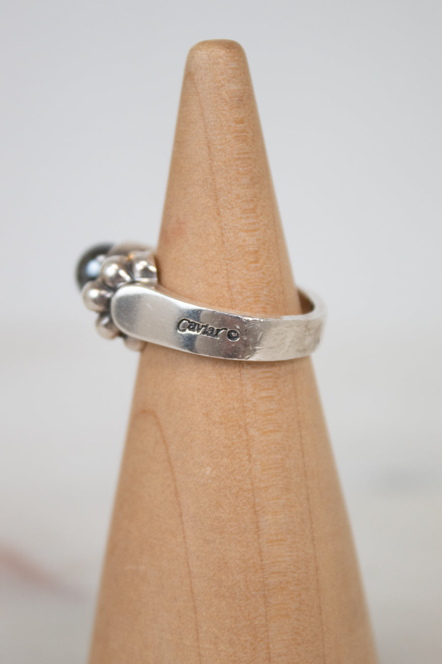 Silver ring with engraved text on a wooden stand against a light background