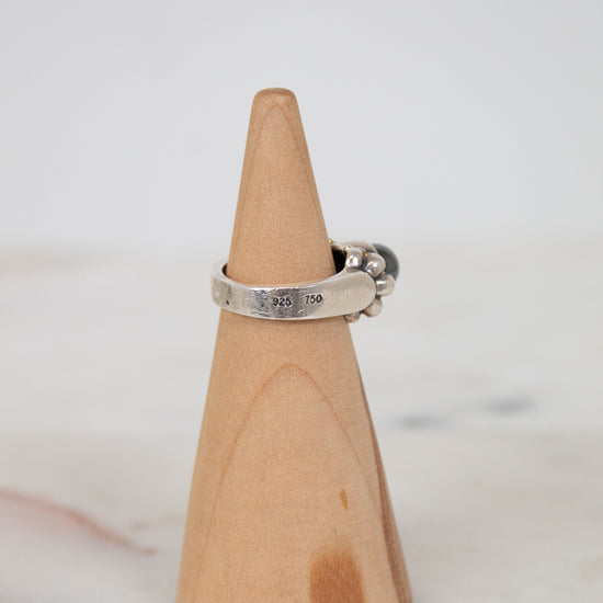 Silver ring on a wooden cone against a light background