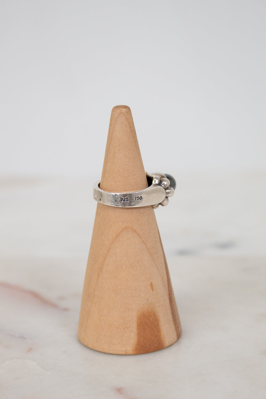 Silver ring on a wooden cone against a light background