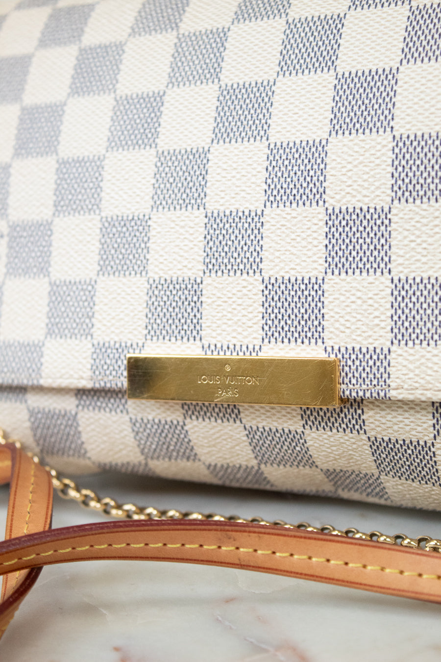 Close-up of a checkered handbag with a gold tag on a marble surface