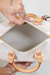 White handbag with gold handles and trim held open by a person.