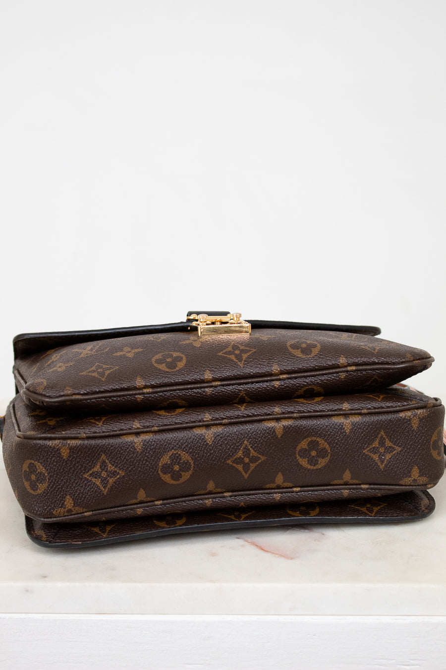 Brown monogram handbag with gold clasp on a white background