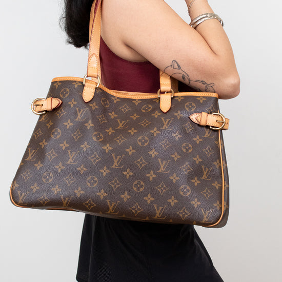 Person holding a Louis Vuitton handbag against a plain background