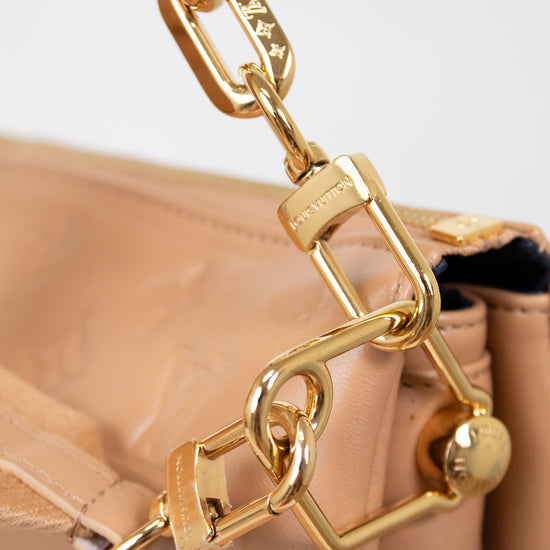 Close-up of a beige handbag with a gold chain handle on a light background