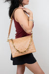 Woman carrying a beige handbag with a gold chain strap on a plain background