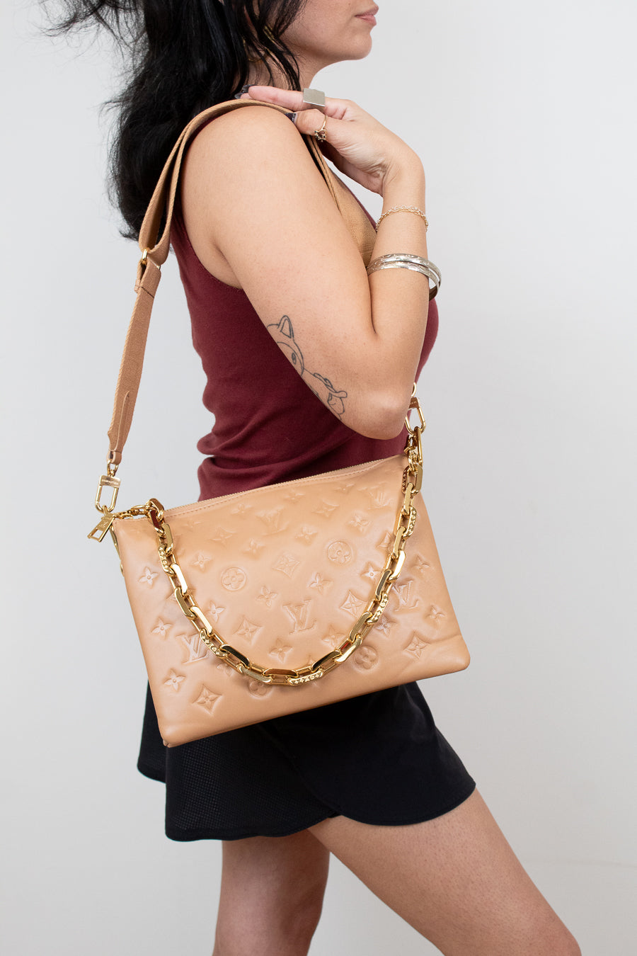 Woman carrying a beige handbag with a gold chain strap on a plain background
