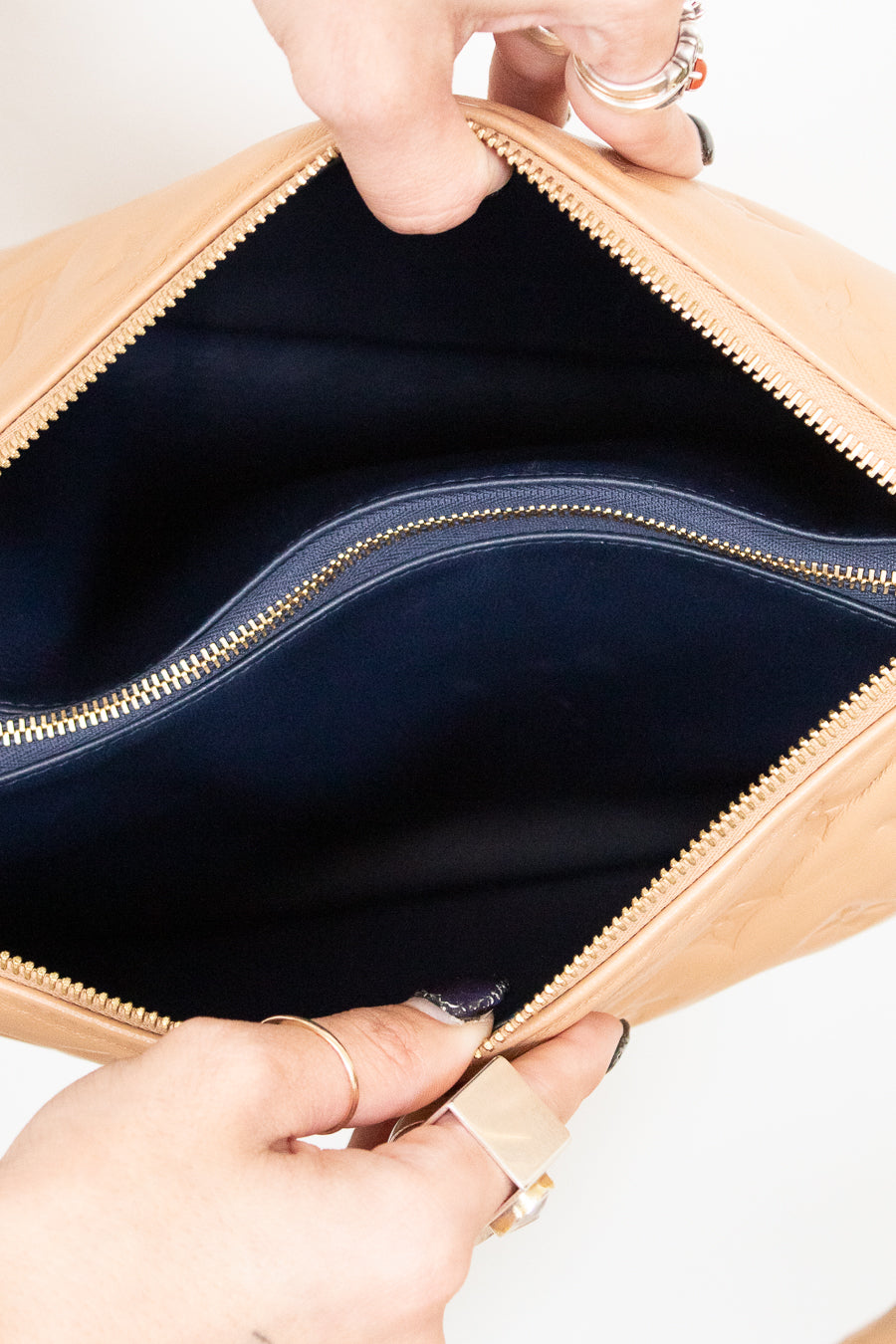 Close-up of a beige handbag with a gold zipper being held open by hands.