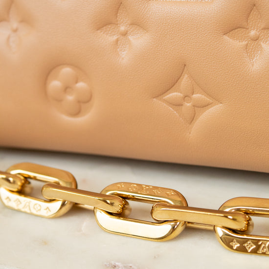 Close-up of a beige handbag with gold chain detail on a marble surface