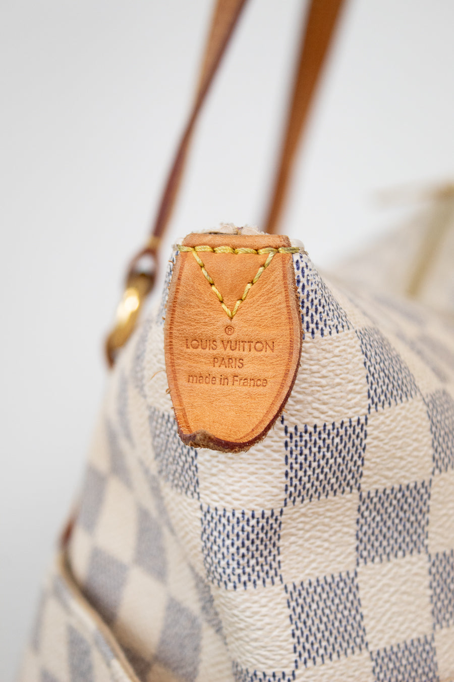 Louis Vuitton handbag with checkered pattern and brown leather tag.