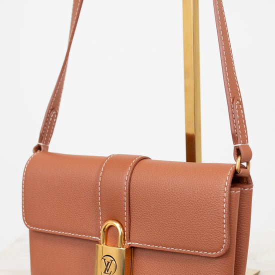Brown leather handbag with gold lock on a white background