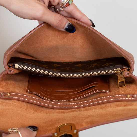 Brown leather handbag held by a person with visible jewelry against a plain background