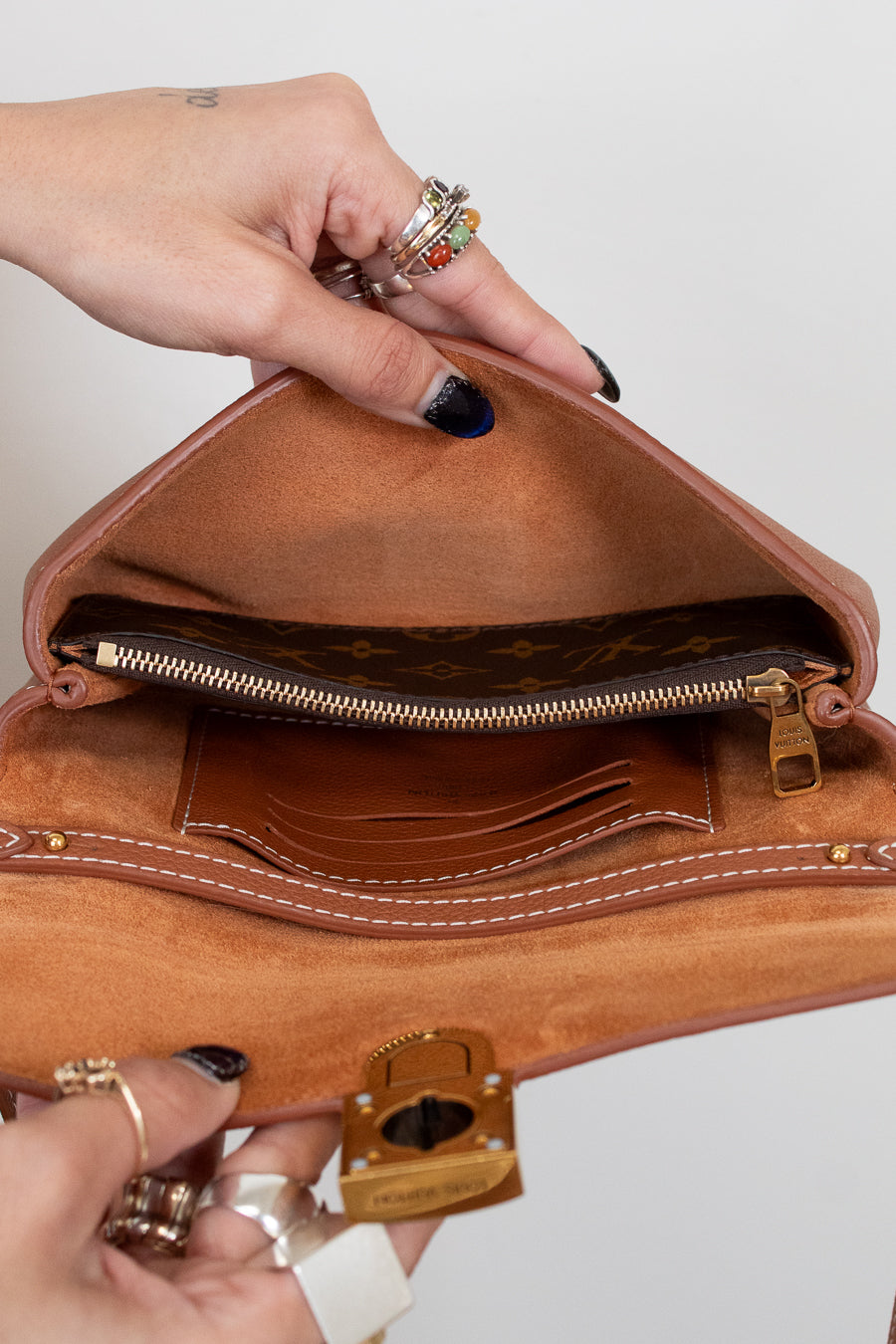 Brown leather handbag held by a person with visible jewelry against a plain background