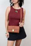 Woman wearing a burgundy sleeveless top and black skirt, holding a brown handbag against a plain background.