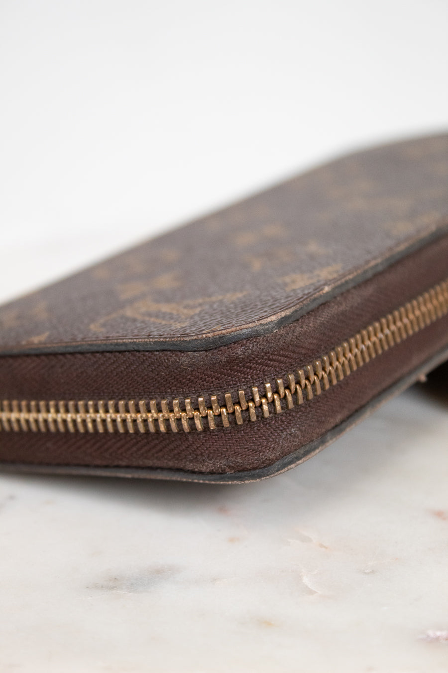 Brown leather wallet with gold zipper on a light marble background
