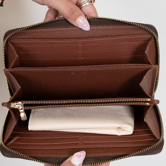 Brown wallet with gold zipper held open by hands on a light gray background