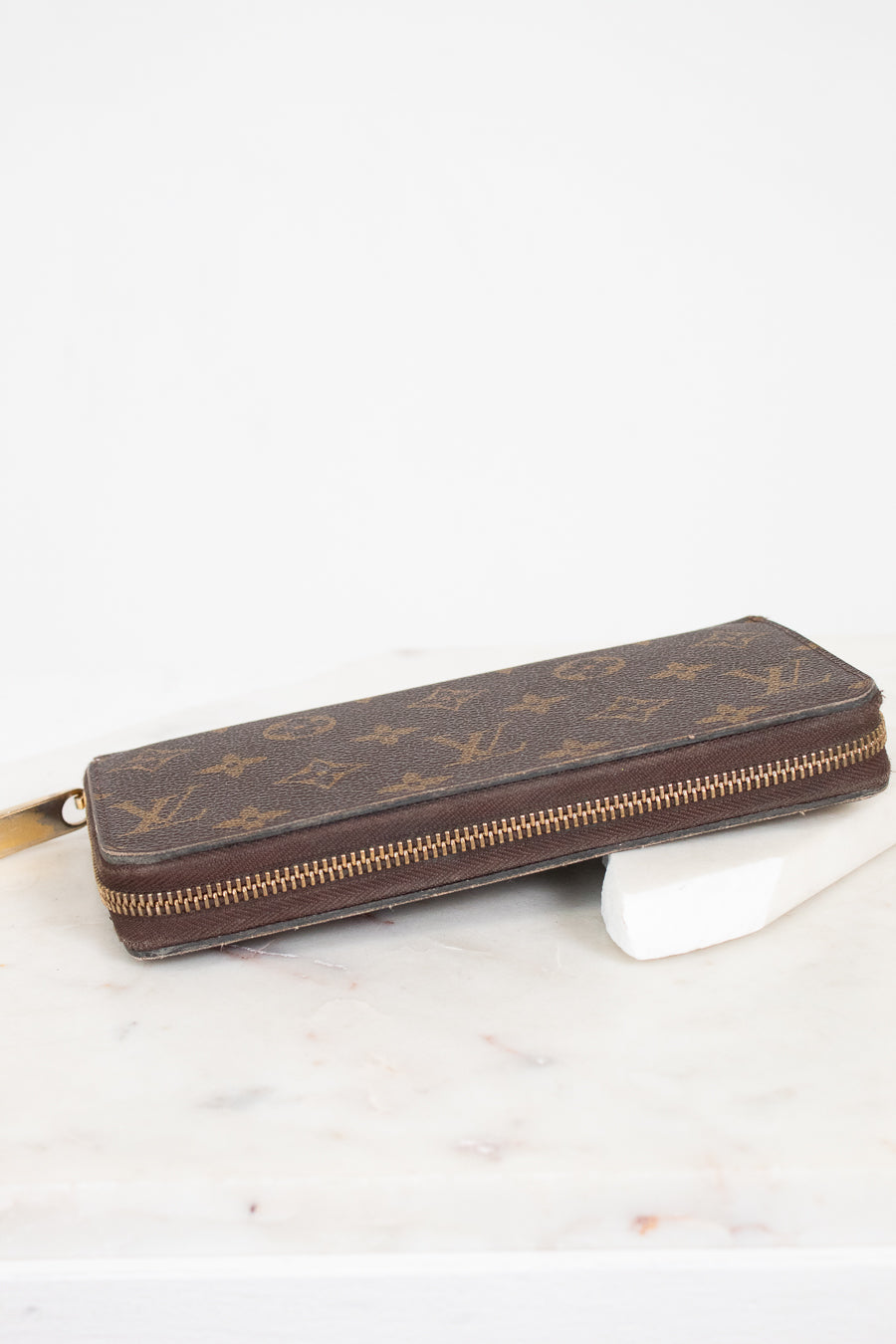 Brown wallet with gold zipper on a white marble surface