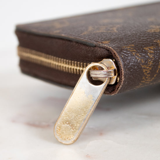 Close-up of a brown wallet with gold zipper pull on a light background