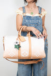 Person holding a beige handbag with floral design, wearing denim overalls.