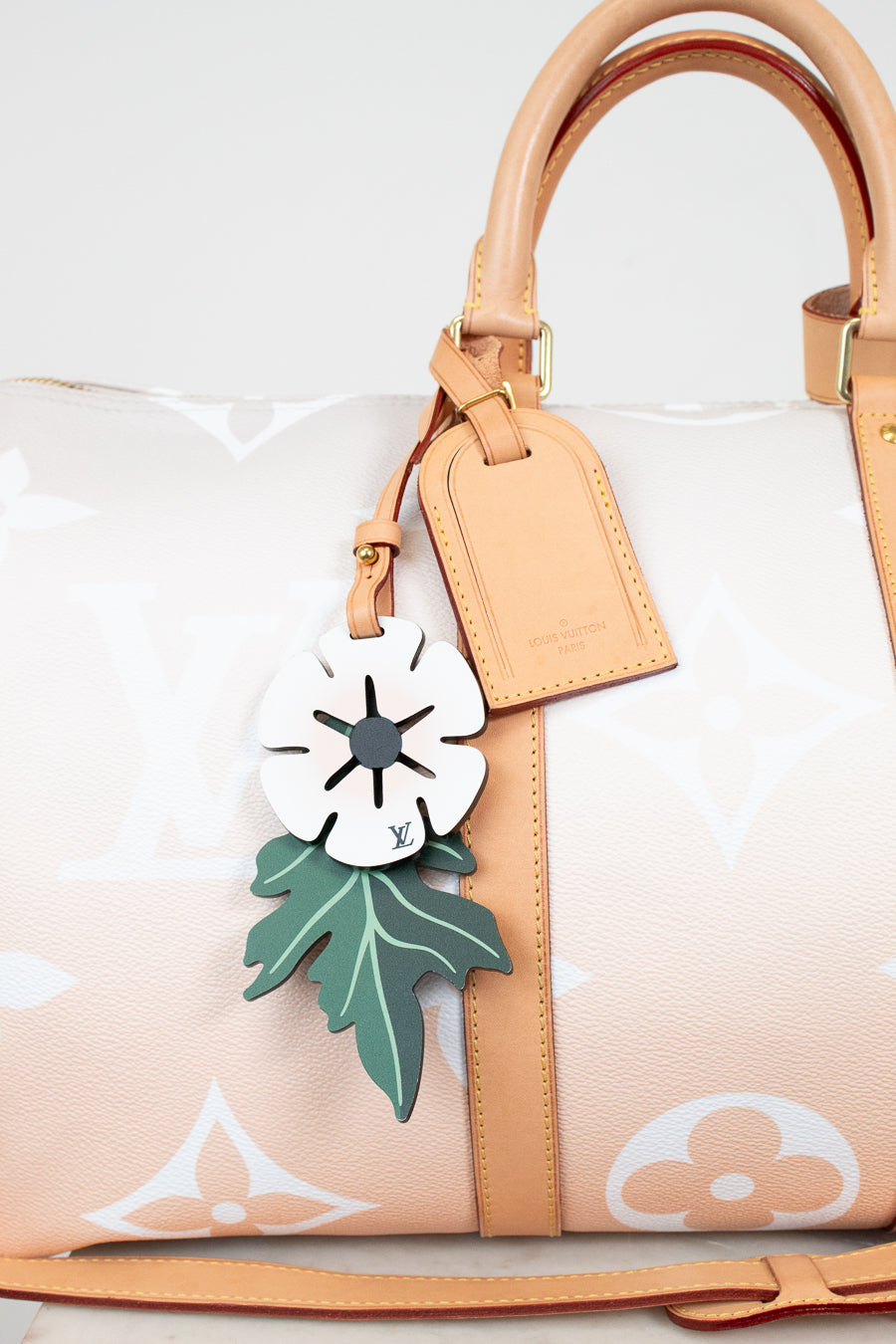 Handbag with a decorative tag featuring a white flower and green leaves on a light background