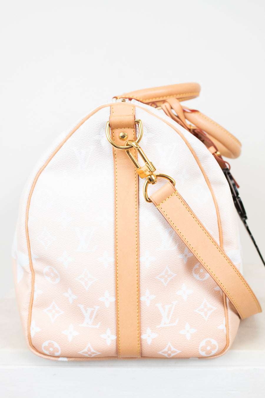 Side view of beige duffle bag with tan leather trim on white background