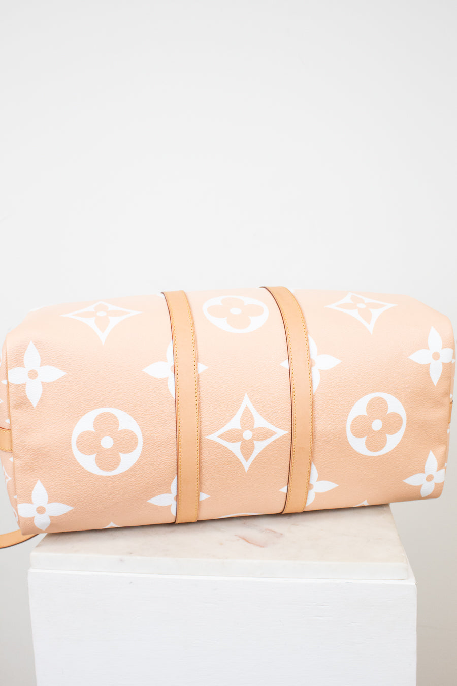 Bottom view of beige duffle bag with white monogram pattern on a light gray background