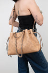 Person holding a beige handbag with a chain detail against a plain background