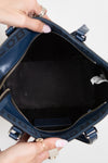 Blue handbag with a visible brand logo, held open by hands.