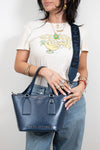 Person holding a blue handbag with visible branding, wearing a white t-shirt with a graphic design.