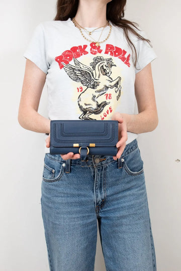 Person wearing a graphic t-shirt and holding a blue wallet against a plain background