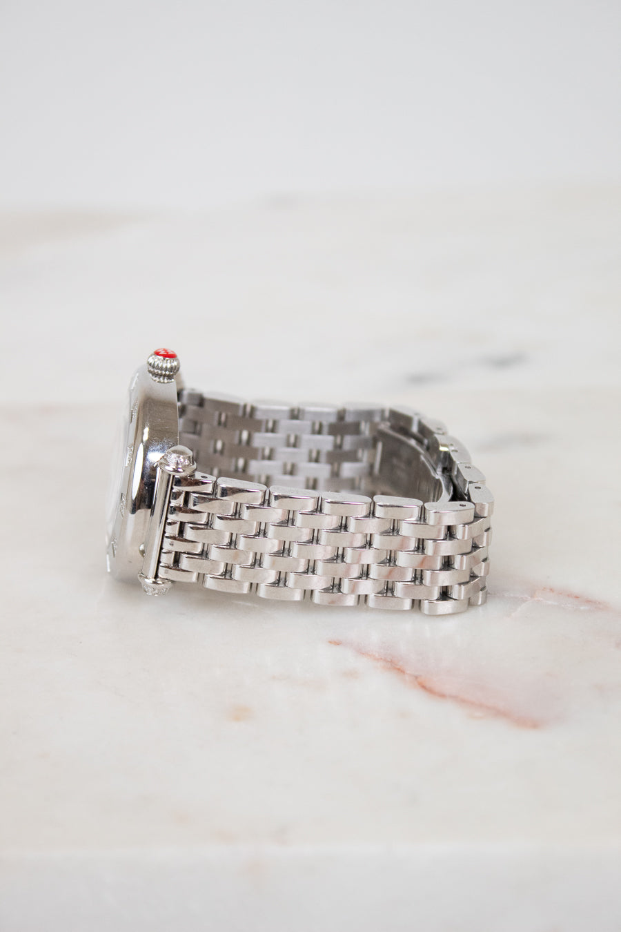 Silver watch with a woven metal strap on a light marble background