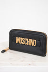 Black wallet with gold 'Moschino' logo on a white marble surface