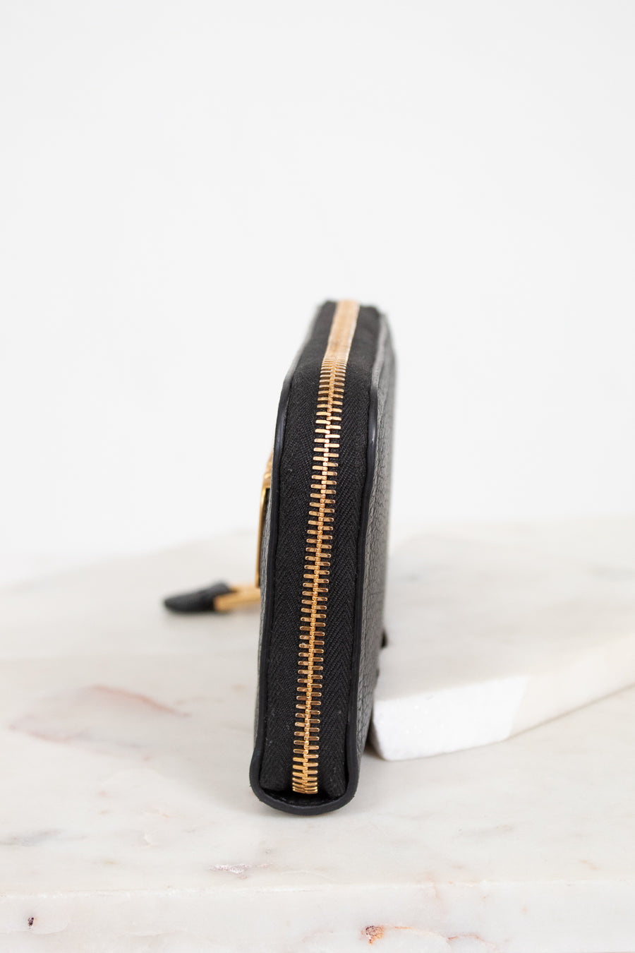 Black wallet with gold zipper on a white marble surface