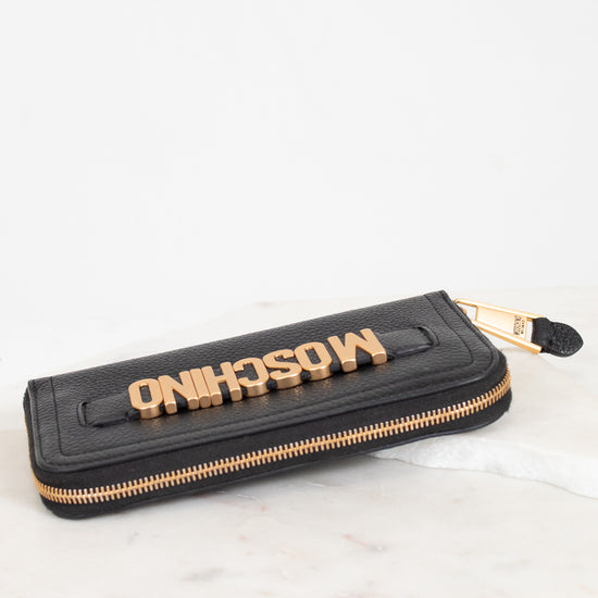 Black wallet with gold zipper and 'Moschino' branding on a white background