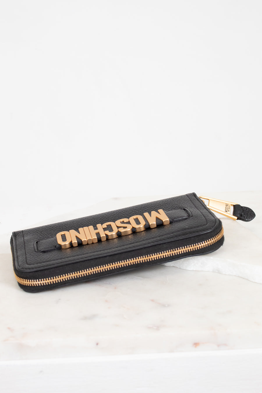 Black wallet with gold zipper and 'Moschino' branding on a white background