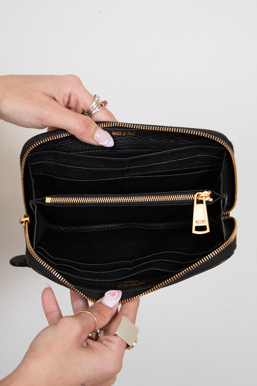 Hands holding open black wallet with gold zipper and card slots on white background