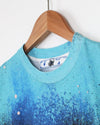 Blue splatter paint pattern on a shirt with a brand label on a wooden hanger against a white background