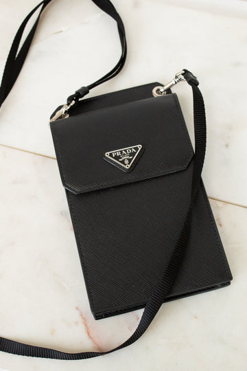 Black Prada handbag with a strap on a light marble background