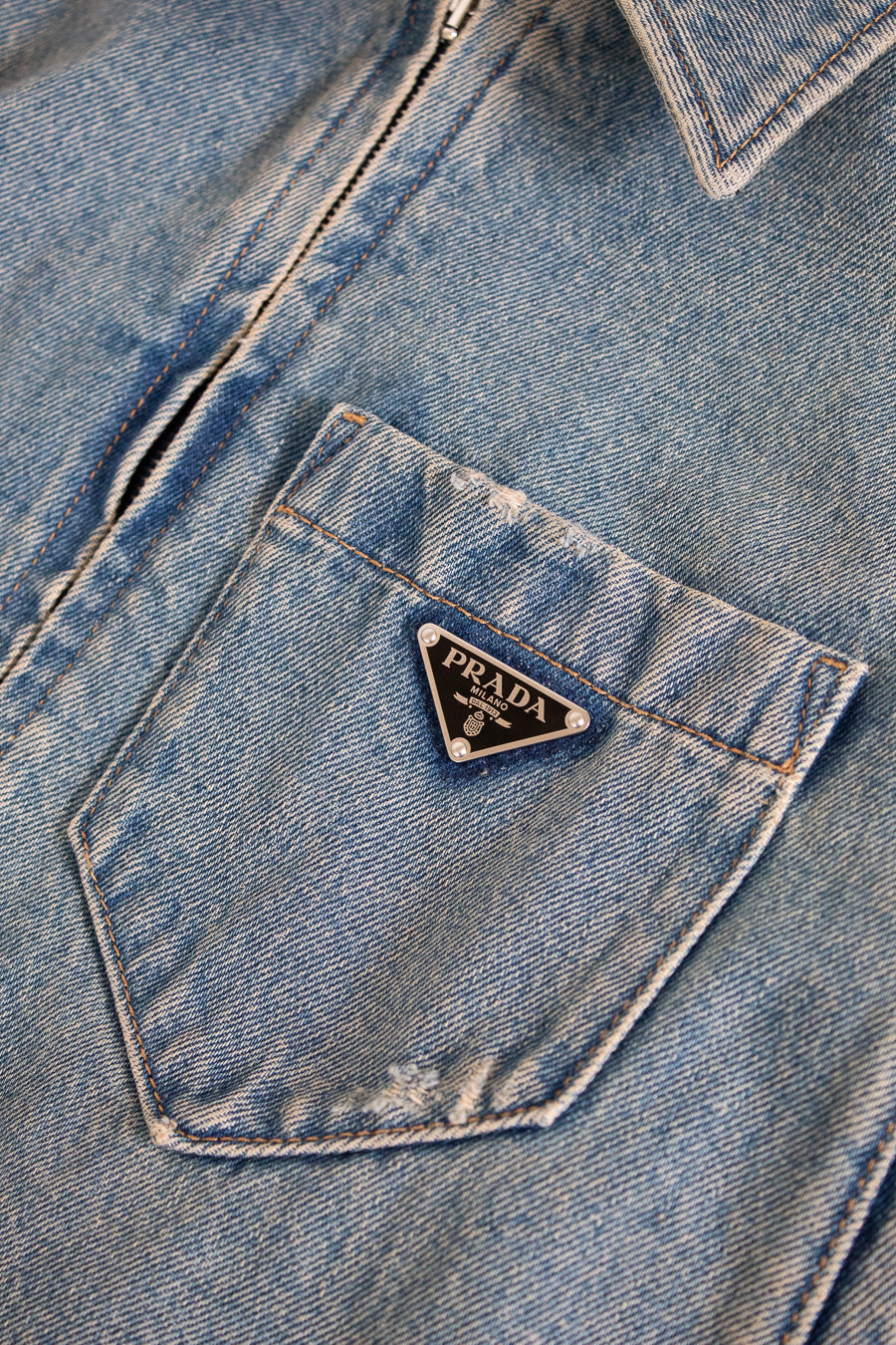 Close-up of a blue denim jacket with a Prada logo on the pocket.