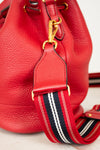 Red leather bucket bag with a striped strap on a light background